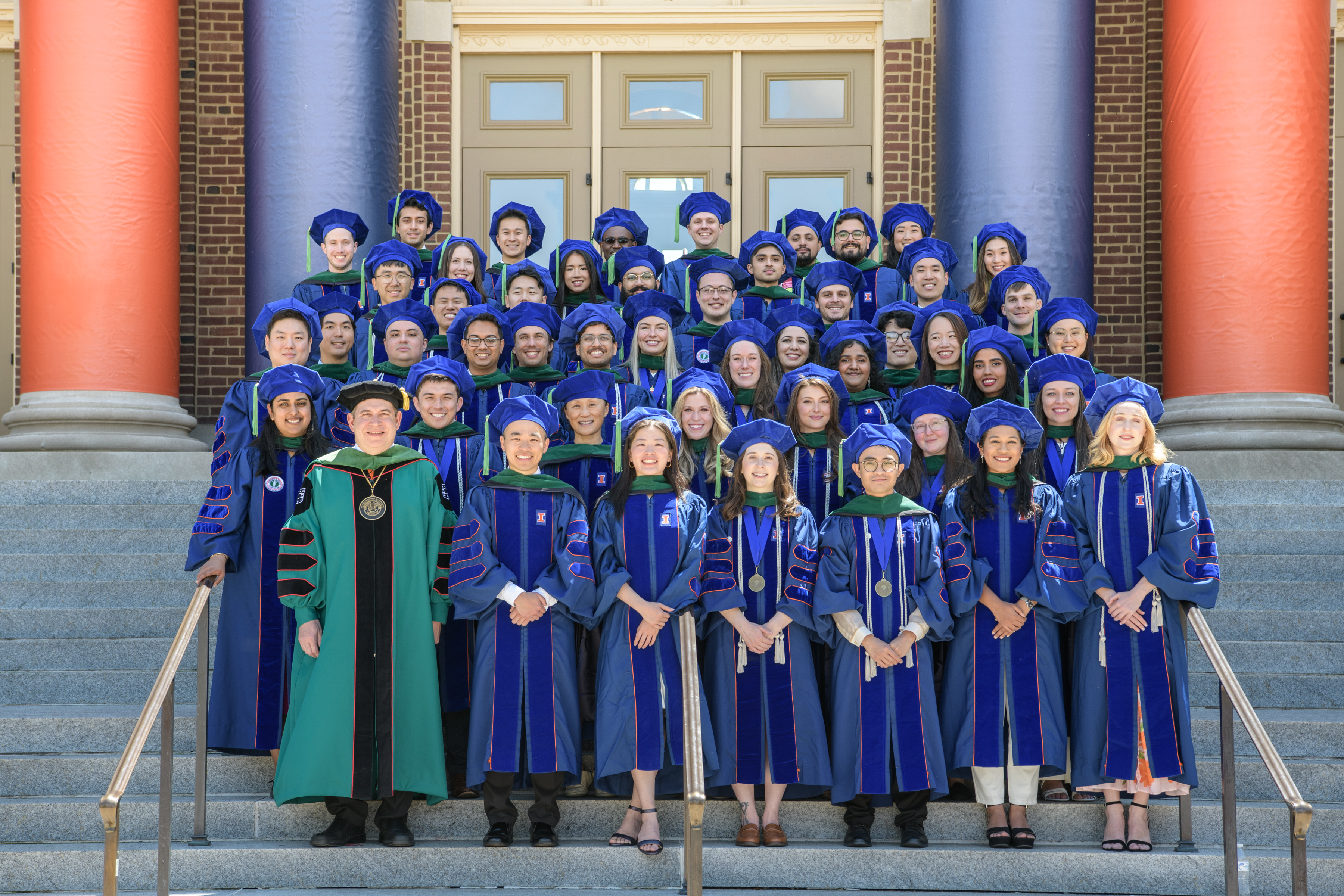 The Carle Illinois College of Medicine Class of 2026 is pictured in their convocation regalia on the steps of Foellinger Auditorium with Dean Mark Cohen.