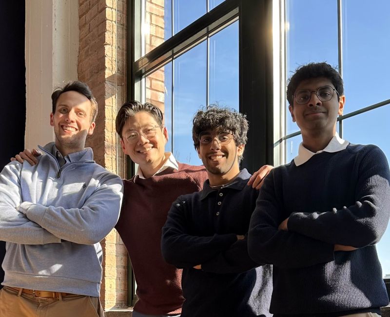 A group photo of Kevin Volkema, DO, MBA;  Richie Li, MD; Satyansh Yeluri; and CEO Rishab Veldur standing in front of a window, smiling at the camera