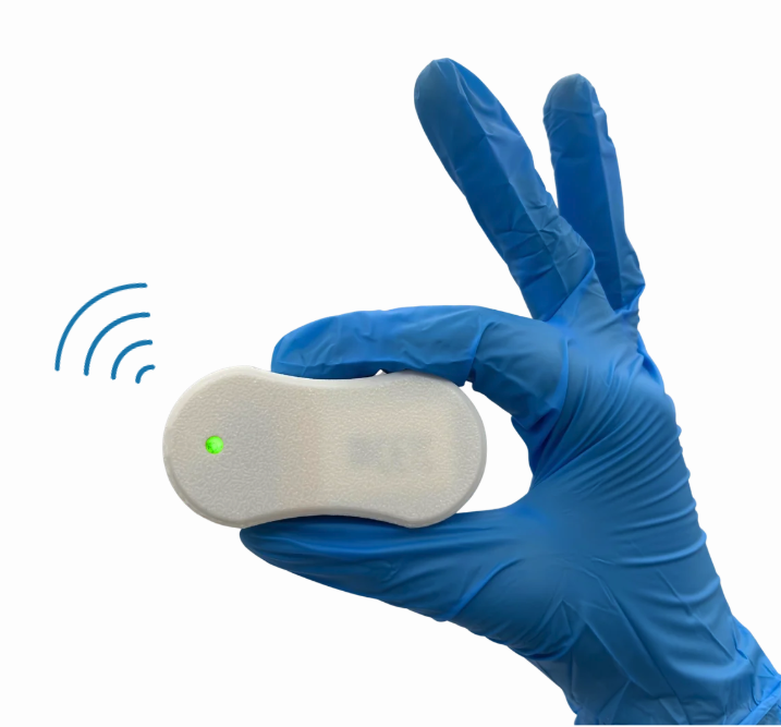A gloved hand holds a small ultrasound device that appears to be emitting a signal. It has an illuminated green indicator light.